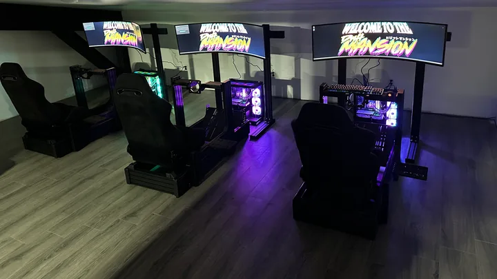Three seated simulator stations with curved monitors showing the Drift Mansion title screen, and an illuminated custom PC beside each seat